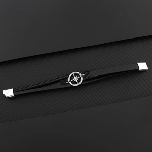 Detail of hand-woven black leather bracelet with metal compass star charm on textured surface