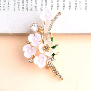 Vintage floral rhinestone brooch with pink petals and green leaves on a book