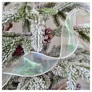 Close-up of iridescent white Christmas ribbon with green and purple glow on a snowy tree