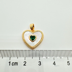 Macro detail of heart pendant with white shell and green gemstone inlay next to a ruler
