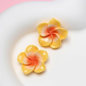 Detailed view of yellow and orange resin frangipani flower charms for DIY accessories