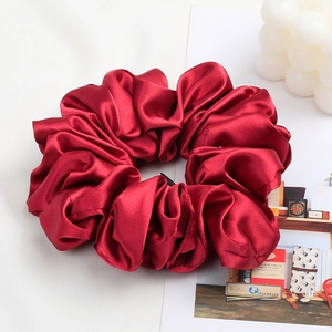 Detail of a large deep red satin scrunchie with silk texture and elegant pleated design