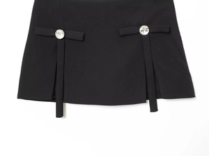 Detailed view of black mini skirt featuring rhinestone buttons and bow tie accents
