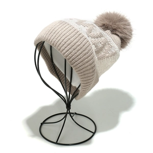 Close-up of cable knit beanie with large faux fur pom-pom on metal stand