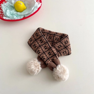 Detail of a brown checkered knit scarf for children featuring soft beige pom-poms