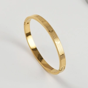 Macro shot of gold stainless steel bangle with music notes and staff engraving