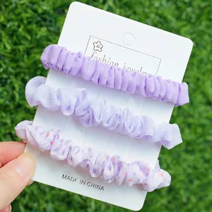 Gros plan de trois chouchous violets aux textures variées sur une carte de présentation