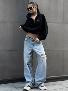 Detail of black half-zip hoodie featuring white letter print styled with ripped jeans