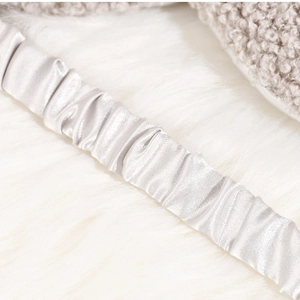 Detail of silver silk satin elastic strap on a plush sleep mask with soft texture