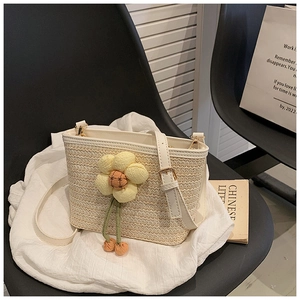 Detail of woven straw bucket bag with floral charm and adjustable white strap