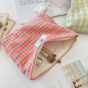 Pochette per cosmetici in tela a quadri rossi con trucchi su una scrivania