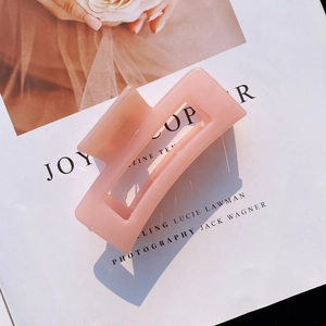 Detail shot of a matte pink rectangular hair claw clip placed on a fashion magazine