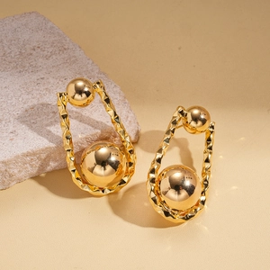Detalle de pendientes en forma de U bañados en oro de 18K con esfera sobre beige