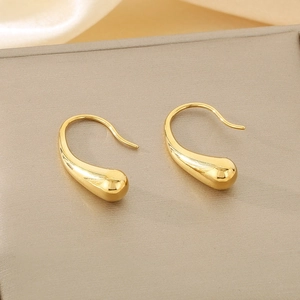 Macro shot of minimalist gold water drop earrings on soft silk and textured background