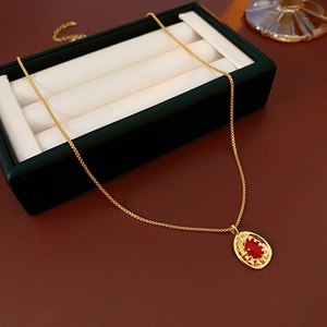 Detail of vintage gold oval necklace with a red gemstone and sunburst engraving