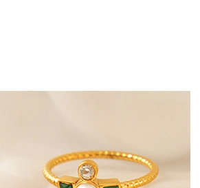 Close-up of a gold twisted ring featuring a green square gem, white stone, and pearl