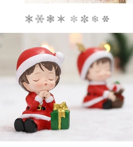 Close-up of resin Christmas boy figurine in red outfit praying next to green gift box