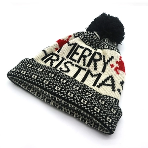 Detail of knit Christmas hat with black pom-pom and Merry Christmas elk pattern