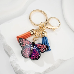 Detail of a butterfly charm keychain with colorful tassels on a white stone background