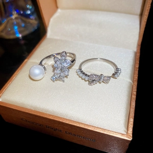 Close-up of zircon bow and pearl open rings set in a luxury champagne satin jewelry box