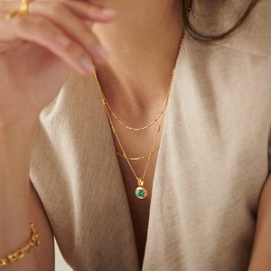 Layered gold necklace featuring a green gemstone pendant worn by a female model