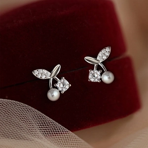 Macro view of cherry-shaped earrings with white pearls and sparkling zircons on red velvet