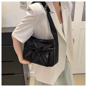 Detail of black glossy pleated shoulder bag with bow decoration and cloud-style strap