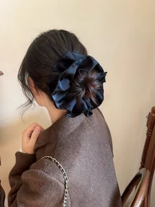Detail of a large black satin scrunchie with ruffled edges worn on a low bun hairstyle