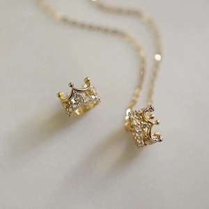 Close-up of luxury gold crown earrings with sparkling cubic zirconia on a warm background