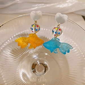 Gros plan de boucles d'oreilles poisson rouge en résine bleue et orange dans un verre