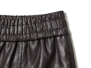 Detail of high waist elastic waistband on deep brown faux leather shorts with lychee texture