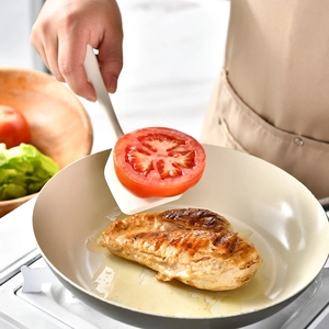 Heat-resistant white silicone spatula flipping tomatoes in a non-stick frying pan