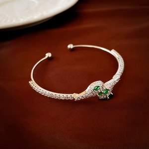 Macro detail of silver snake-shaped open cuff with green marquise stones and zircon paving