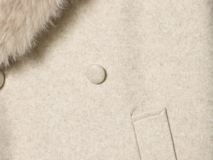 Close-up of beige wool coat with soft faux fur collar and covered button detail