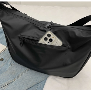 Close-up of black crossbody bag front pocket holding a smartphone for storage scale