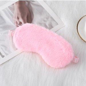 Detailed view of pink plush sleep mask with elastic strap on a cozy white rug