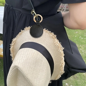 Black leather magnetic hat clip with gold buckle hanging on a black shoulder bag strap