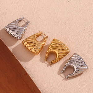 Detailed close-up of gold and silver wave-textured hollow trapezoid earrings on neutral background