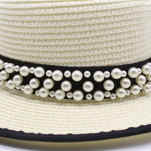 Dettaglio di cappello in paglia con nastro grosgrain nero e perle decorative