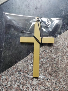 Dettaglio di un ciondolo a croce dorata da sacerdote con cordino nero nella confezione