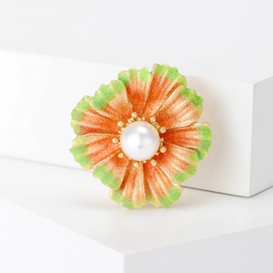 Close-up of orange floral brooch with gradient petals and a white pearl center
