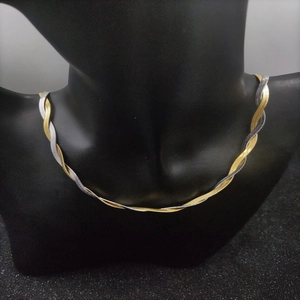 Detail view of a two-tone twisted herringbone snake chain necklace on a black mannequin