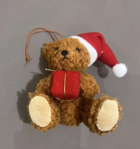 Detailed view of a brown plush Christmas bear with a red hat holding a gift box