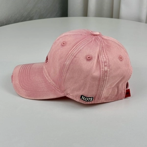 Detail view of pink washed cotton baseball cap with distressed brim and side letter embroidery