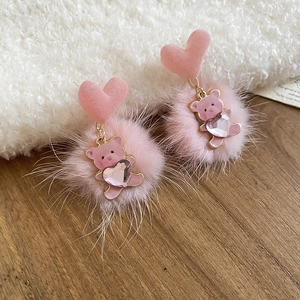 Detail view of pink bear pendant earrings with plush pompom and heart on soft fabric
