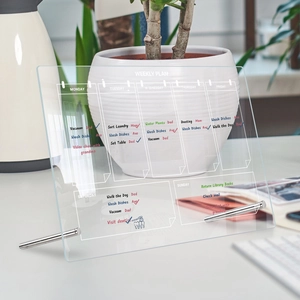 Close-up of clear acrylic weekly plan board with metal stand and handwritten daily tasks