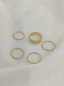 Detail view of 5-piece gold stackable rings set featuring wide and thin bands on white fabric
