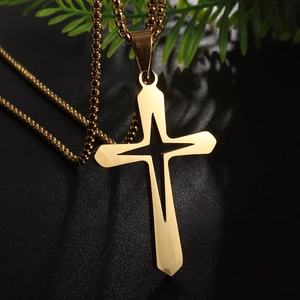 Detail view of a polished gold hollow cross pendant necklace on a black textured background