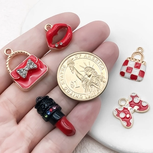 Handmade enamel lipstick and bow charms displayed next to a dollar coin for scale