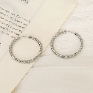 Macro detail of large silver twisted hoop earrings with elegant rope texture for women